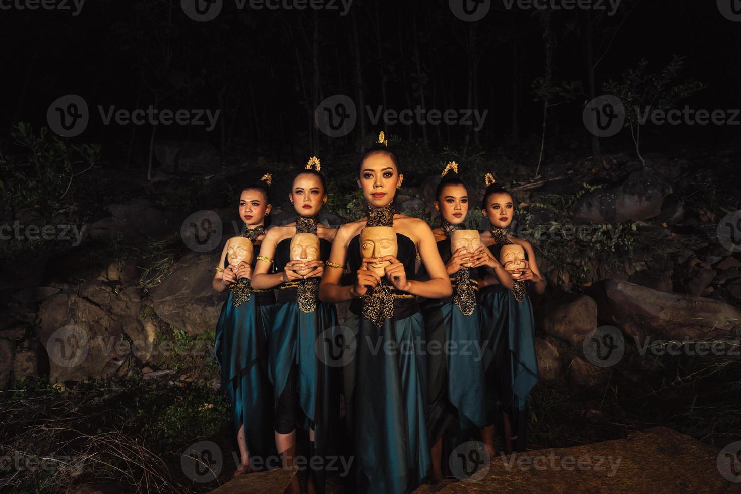 A Group of ethnical women holding a wooden craft mask in their hands while in line inside the wood photo