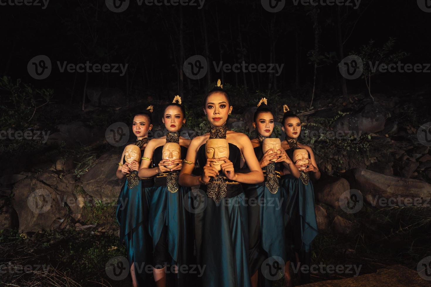 A Group of ethnical women holding a wooden craft mask in their hands while in line inside the wood photo