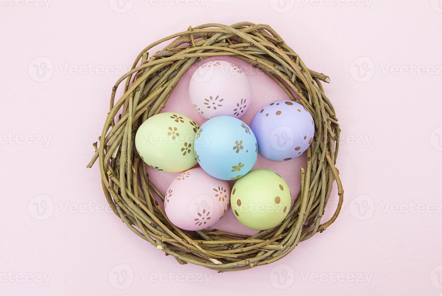 Painted multicolored eggs in wooden nest of branches on pink background. View from above. Easter, birth. Copy space photo