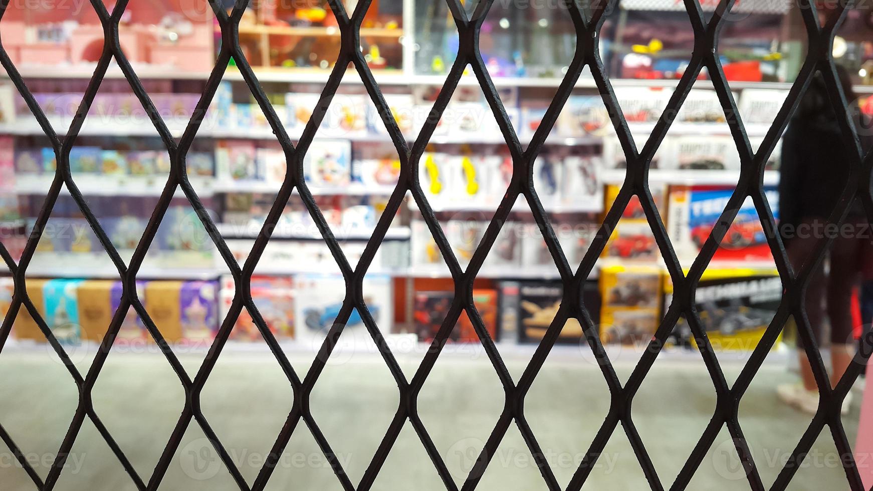Selective focus on chain link fence with blurred background of children's toys on a shelf in a supermarket. Wire mesh fence. photo