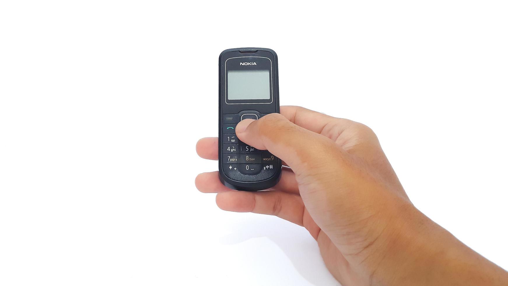 Jakarta, Indonesia, 2023 - Hand holding old Nokia cell phone isolated on white background. Nokia 1202 series. photo