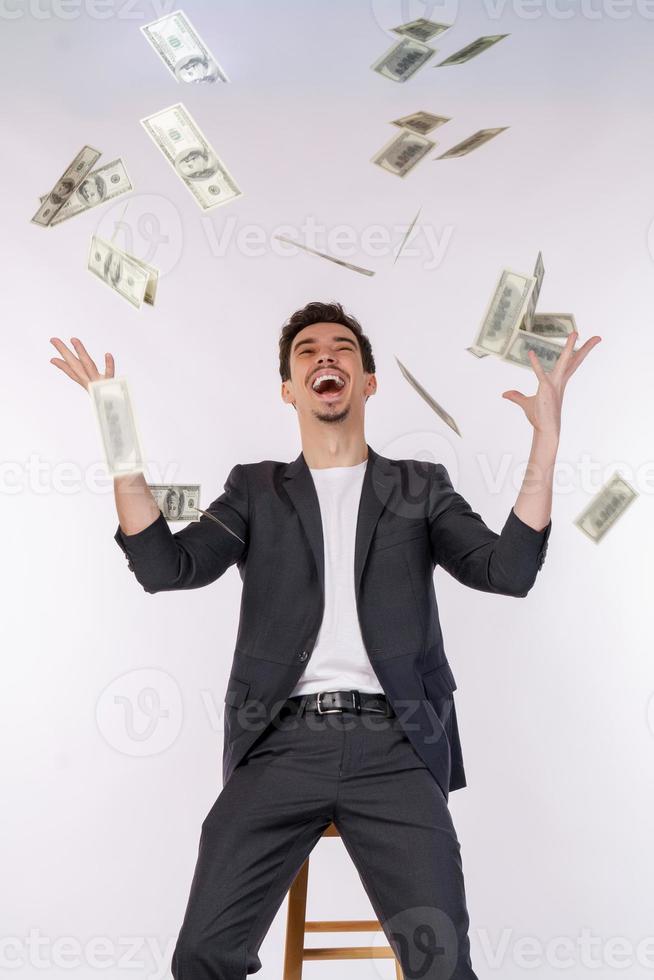 Portrait of happy young man throwing money up while standing isolated background photo
