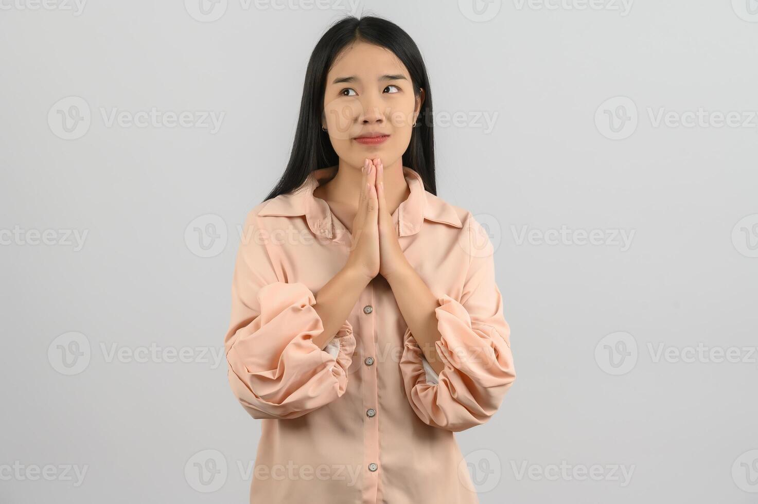 retrato de una joven asiática con camisa rosa rezando con las manos entrelazadas aisladas de fondo blanco foto