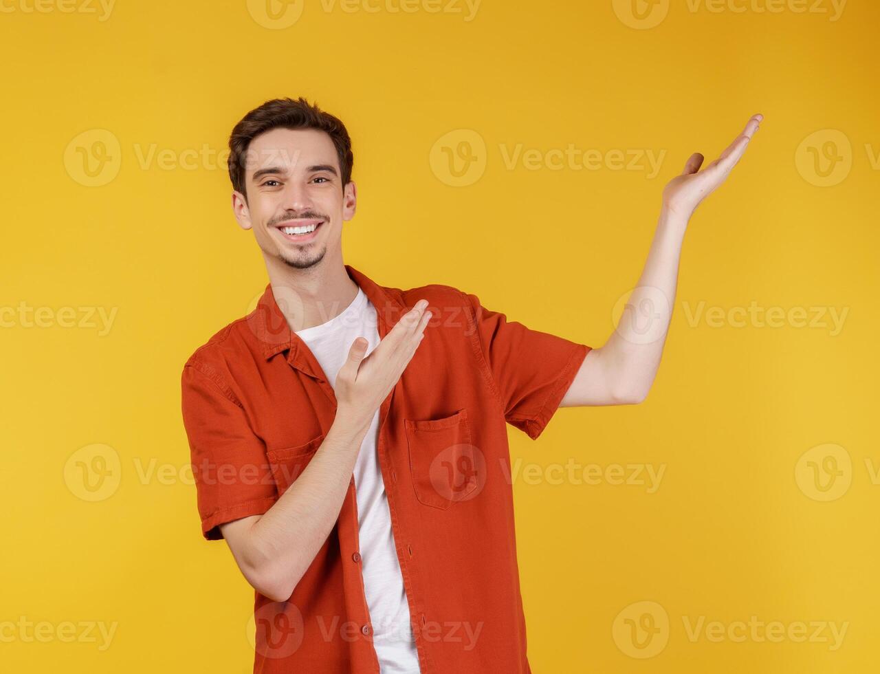 Portrait of happy smiling young man presenting and showing your text or product isolated on yellow background photo