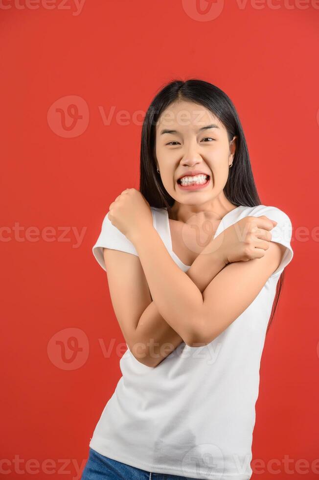 Portrait of Young asian woman in white t-shirt hugging oneself happy and positive isolated on red background photo