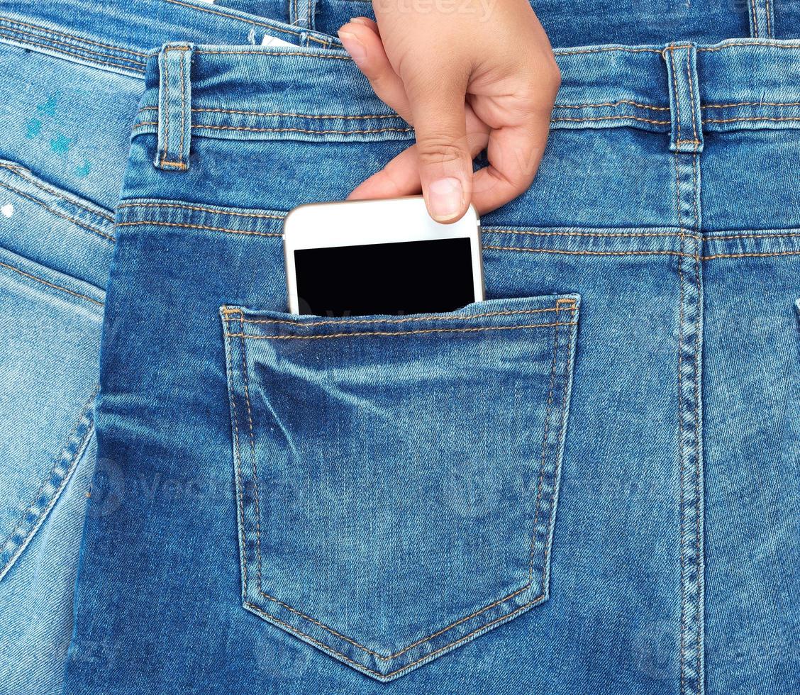 la mano femenina se saca del bolsillo trasero de un smartphone de blue jeans con una pantalla en blanco foto