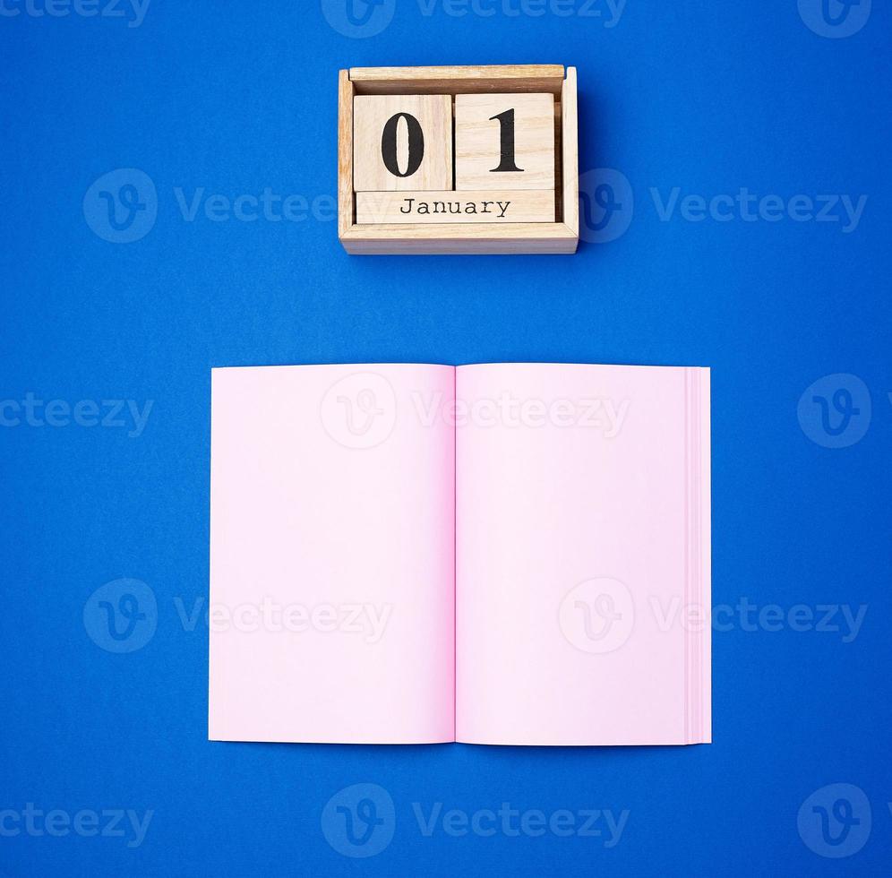 wooden retro calendar with the date of January 1 and an open notebook with empty pink sheets photo