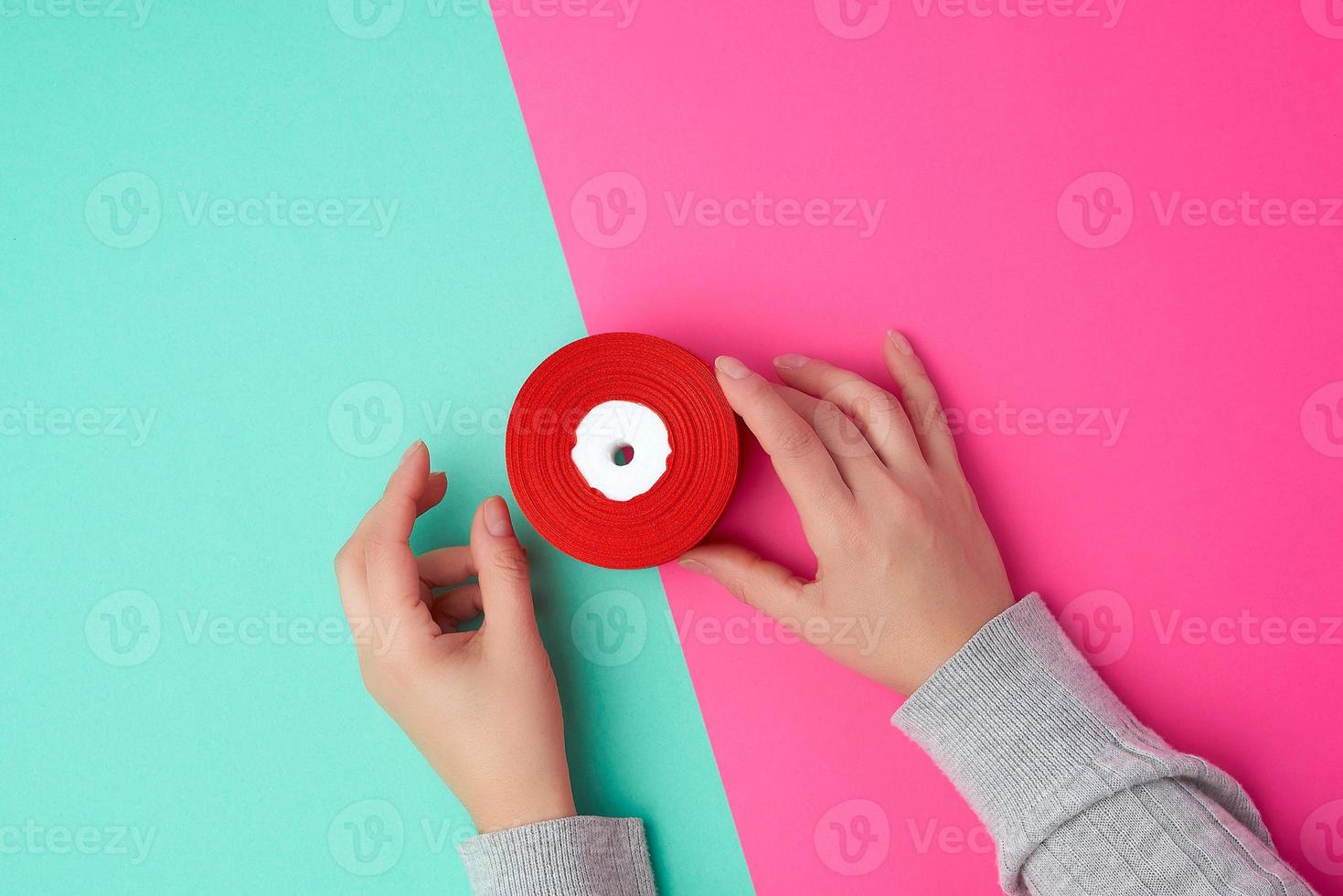 two female hands holding a bobbin with a red silk ribbon photo