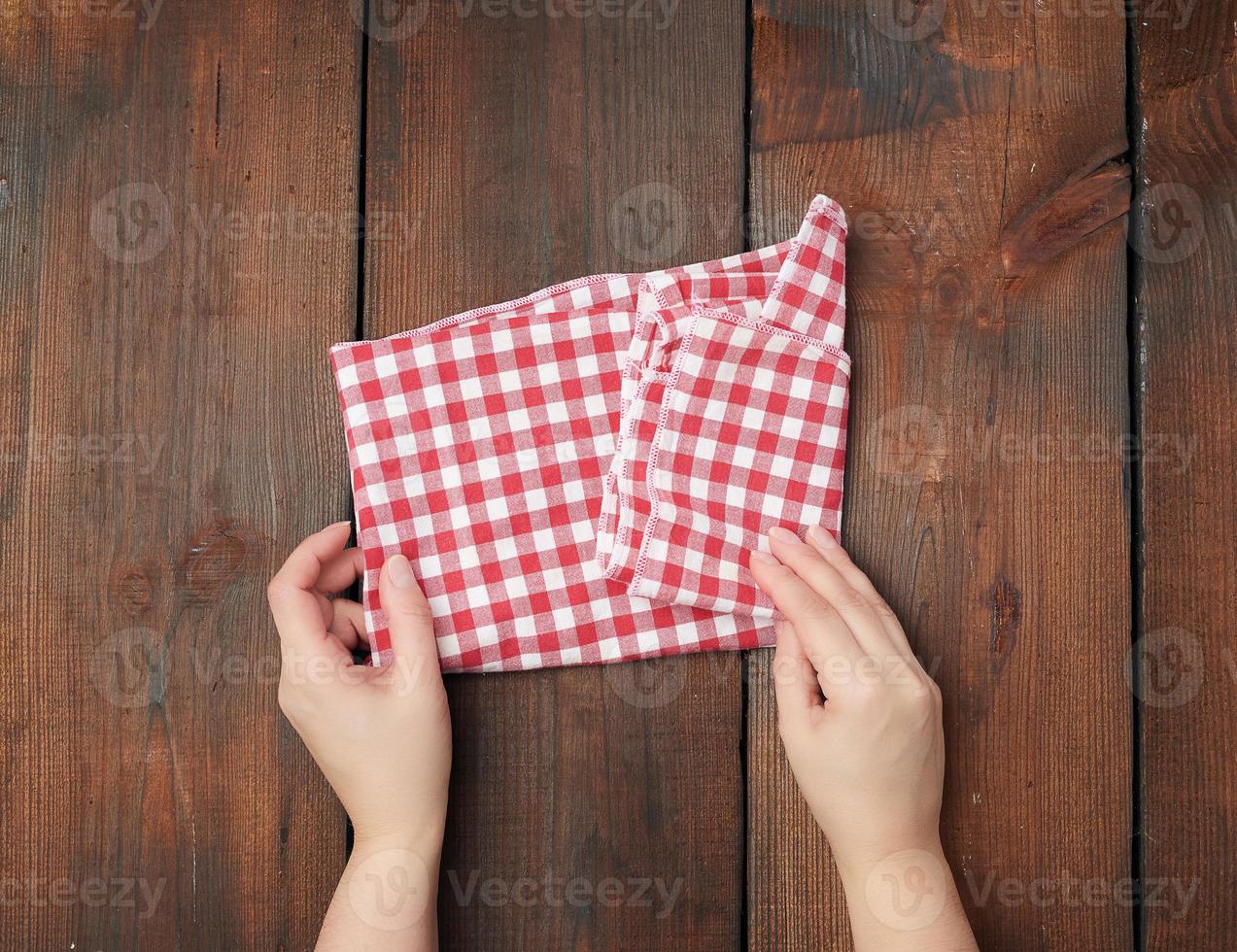 hands hold white red checkered kitchen towel on a brown wooden background photo