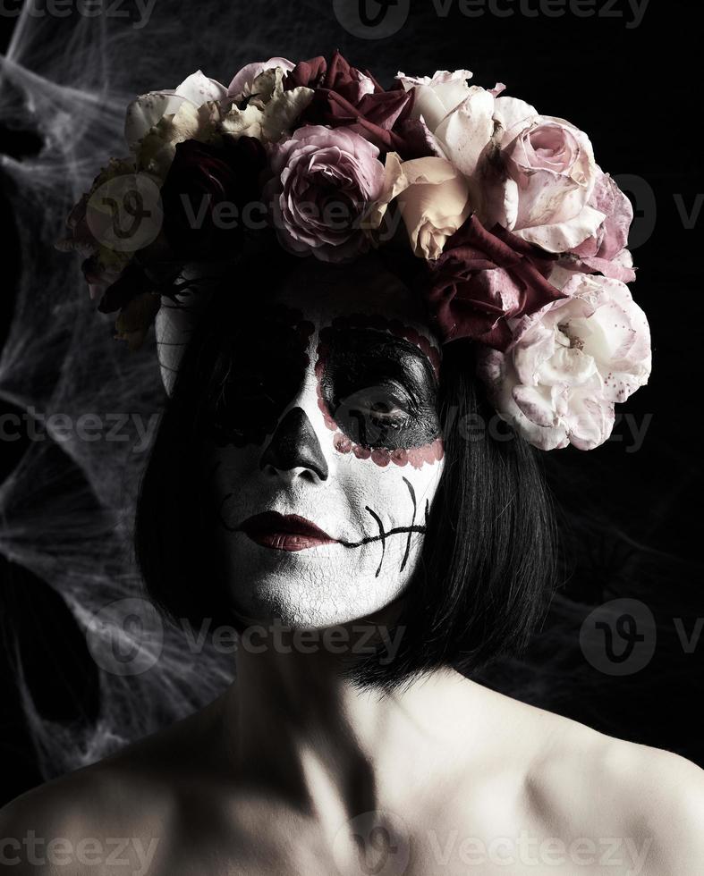 hermosa chica con máscara de muerte tradicional mexicana. calavera catrina. maquillaje de calavera de azúcar. niña vestida con una corona de rosas foto