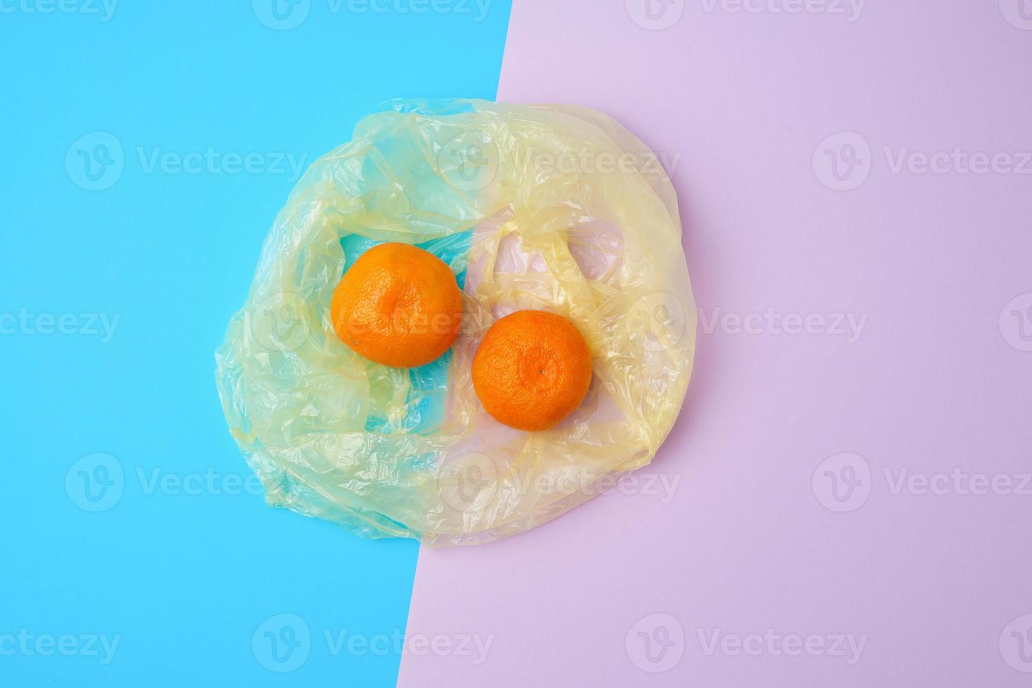 dos mandarinas naranjas maduras yacen en una bolsa de plástico transparente foto