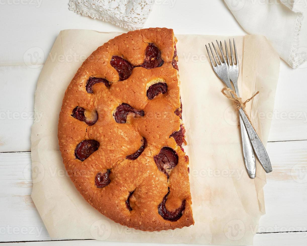 half sponge plum cake on parchment paper and two forks photo