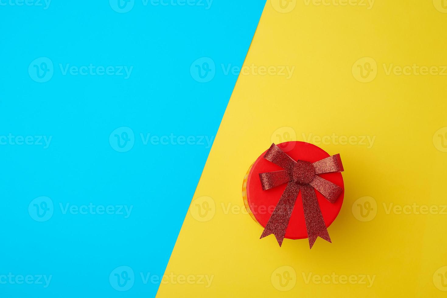 caja roja de cartón redonda con un lazo sobre un fondo azul-amarillo foto