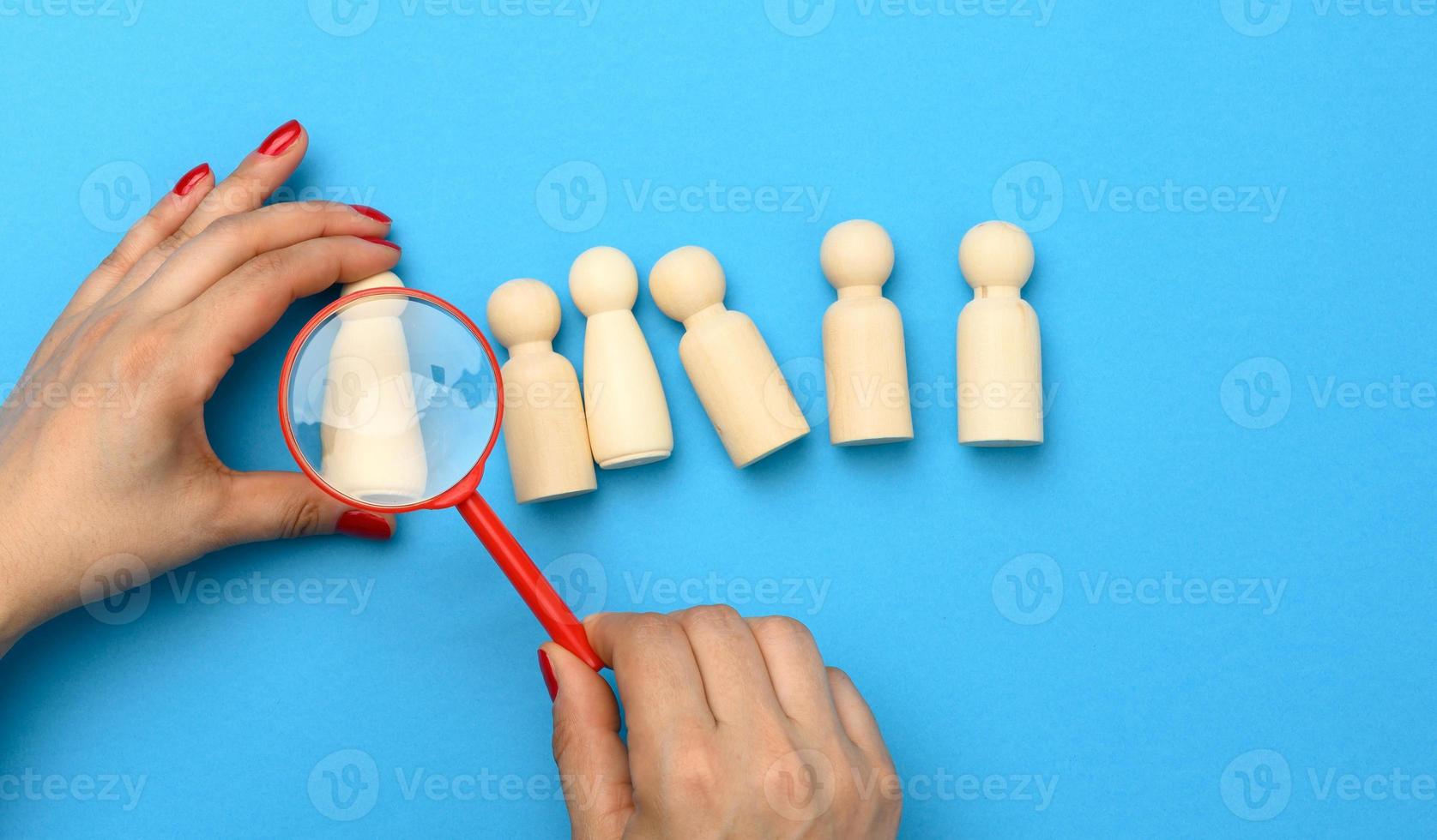 wooden figures of men on a blue background and a red magnifying glass. Recruitment concept, search for talented and capable employees photo