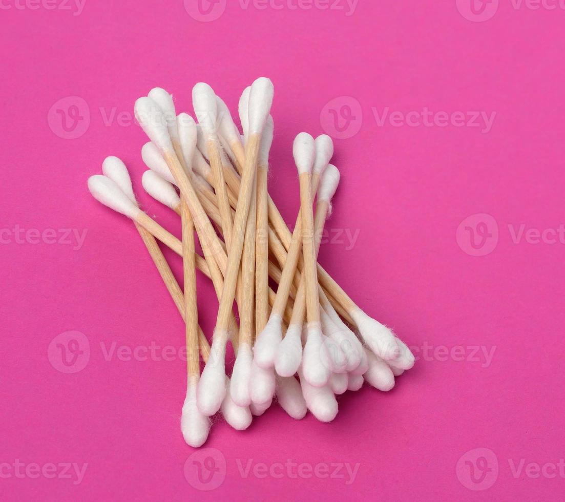 wooden sticks with white cotton wool for the ears on a pink background, hygiene product photo