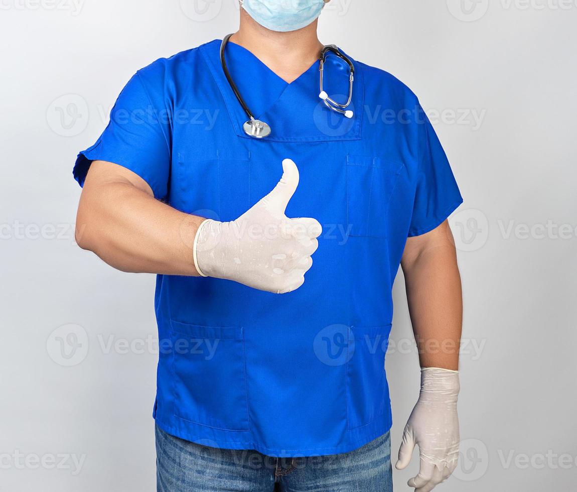 médico masculino con uniforme azul y guantes blancos de látex muestra un gesto con la mano derecha como foto