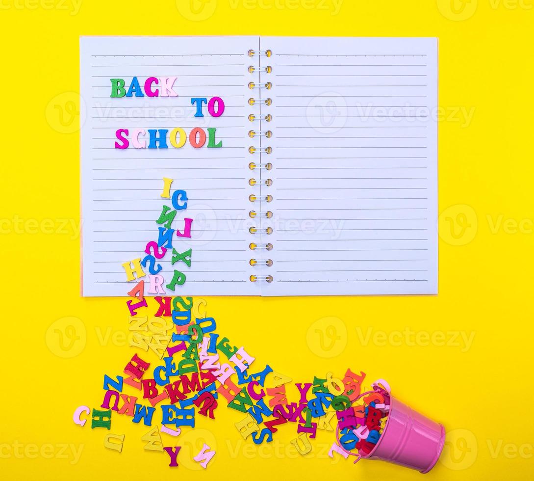 scattered wooden multicolored letters from an iron bucket on a notebook in a line photo