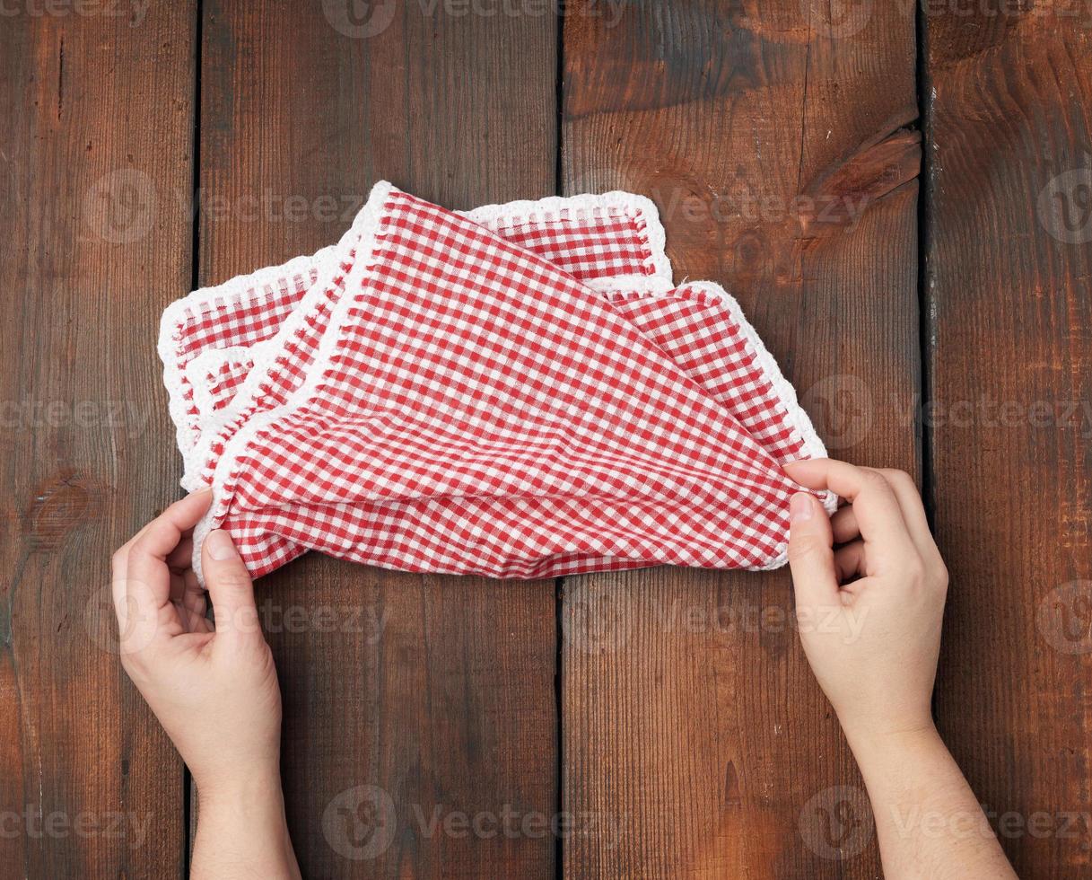hands hold white red checkered kitchen towel on a brown wooden background photo