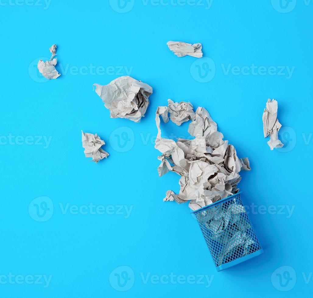 overturned blue metal basket with crumpled pieces of paper photo