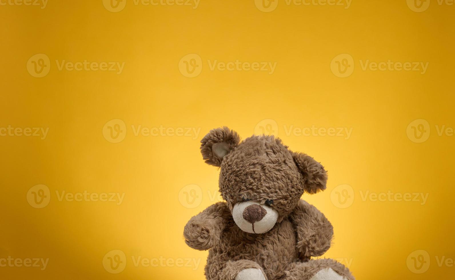 lindo oso de peluche marrón con parches se sienta sobre un fondo amarillo, juguete para niños foto