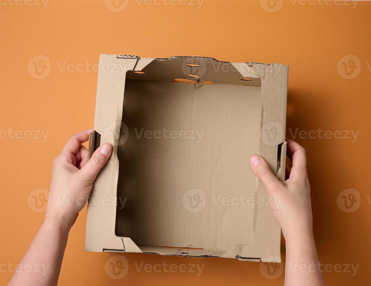 female hands are holding an empty open box of brown cardboard, top view, concept of packing things photo