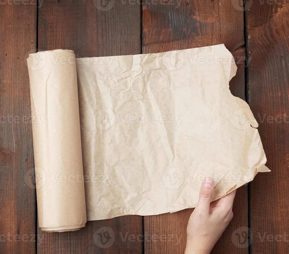 hand holds unfolded roll with brown parchment paper on wooden background photo