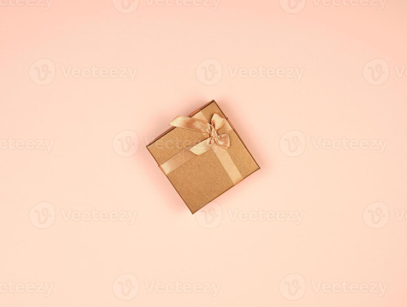 caja de regalo dorada cerrada con un lazo sobre un fondo beige foto