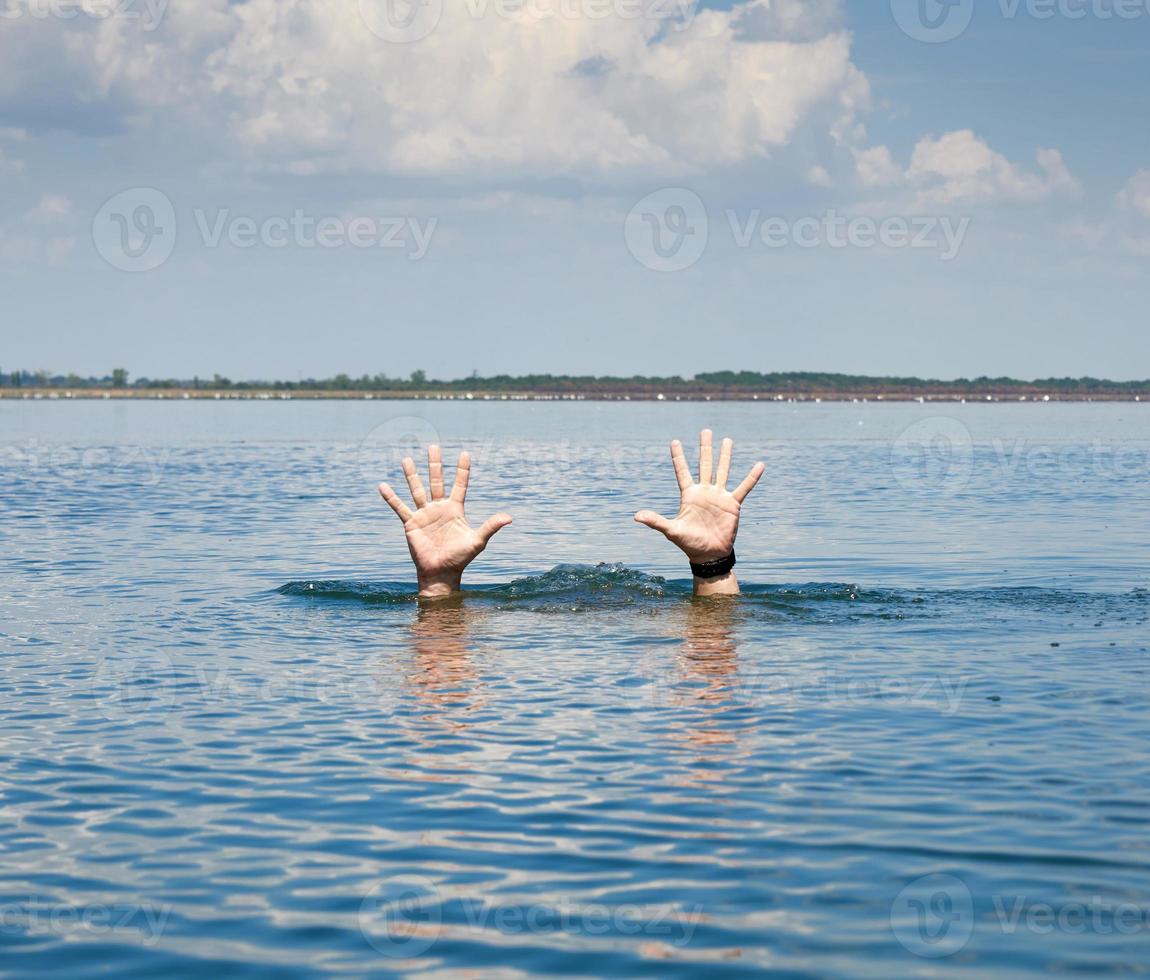 pair of masculine hands sticks out of the sea water on a summer day photo