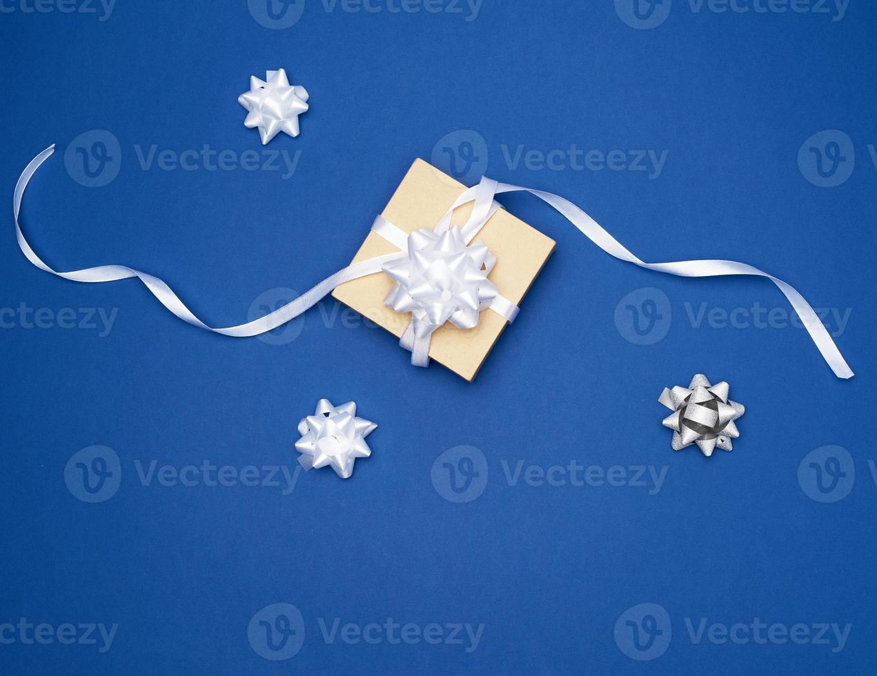 square box with a gift tied with a white ribbon with a bow on a blue background photo