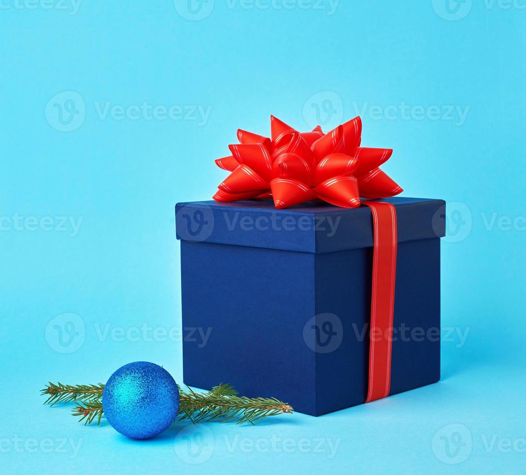 square blue cardboard box with a red bow, sprig of spruce with a shiny blue ball photo