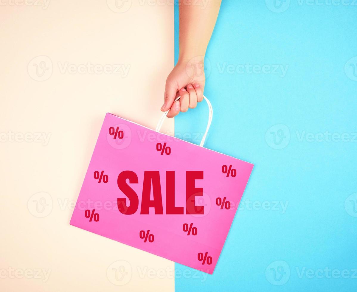 female hand holding a pink paper shopping bag photo