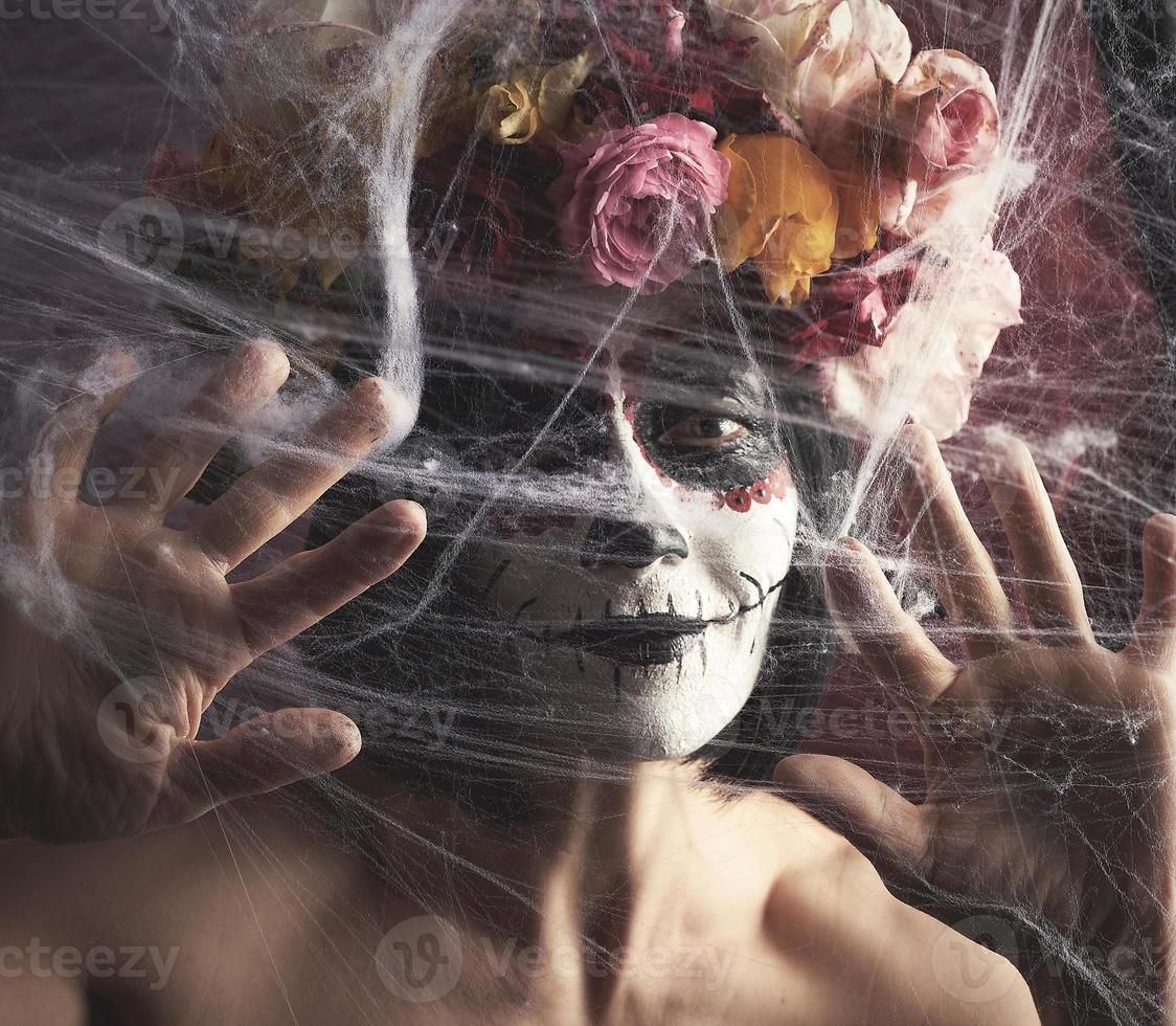 la chica con el pelo negro está vestida con una corona de rosas multicolores y el maquillaje está hecho en su cara calavera de azúcar hasta el día de los muertos foto