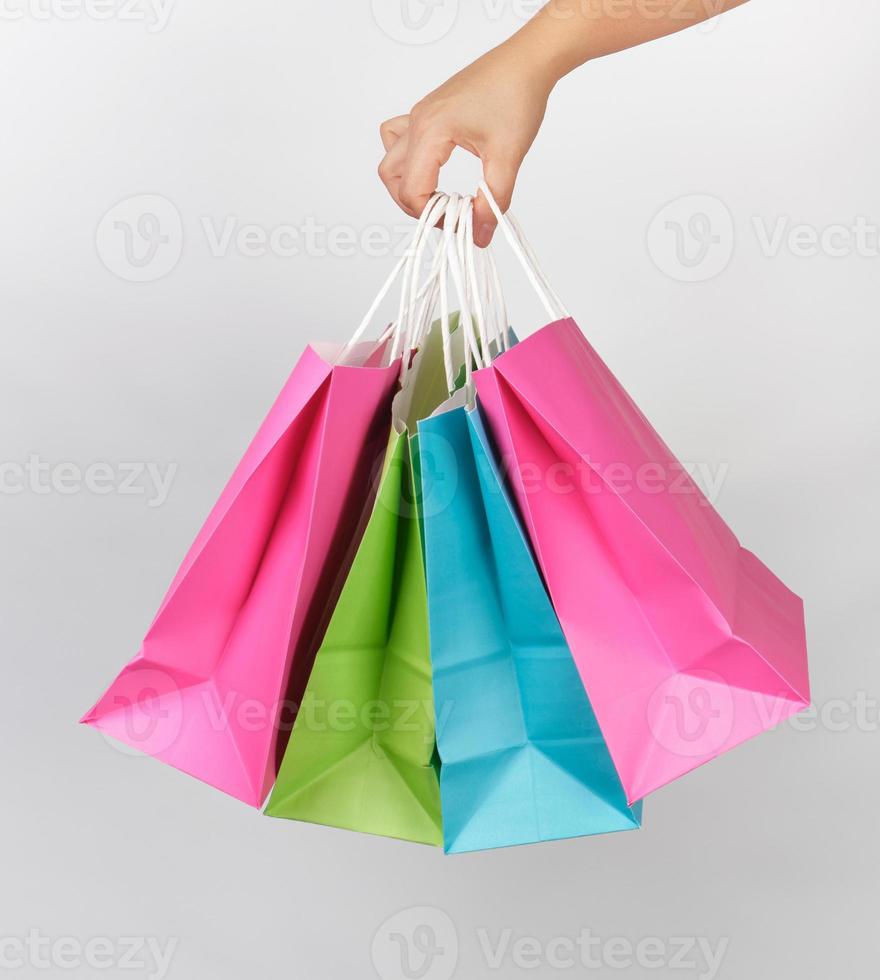 mano femenina sosteniendo cuatro bolsas de embalaje de compras de papel de colores foto