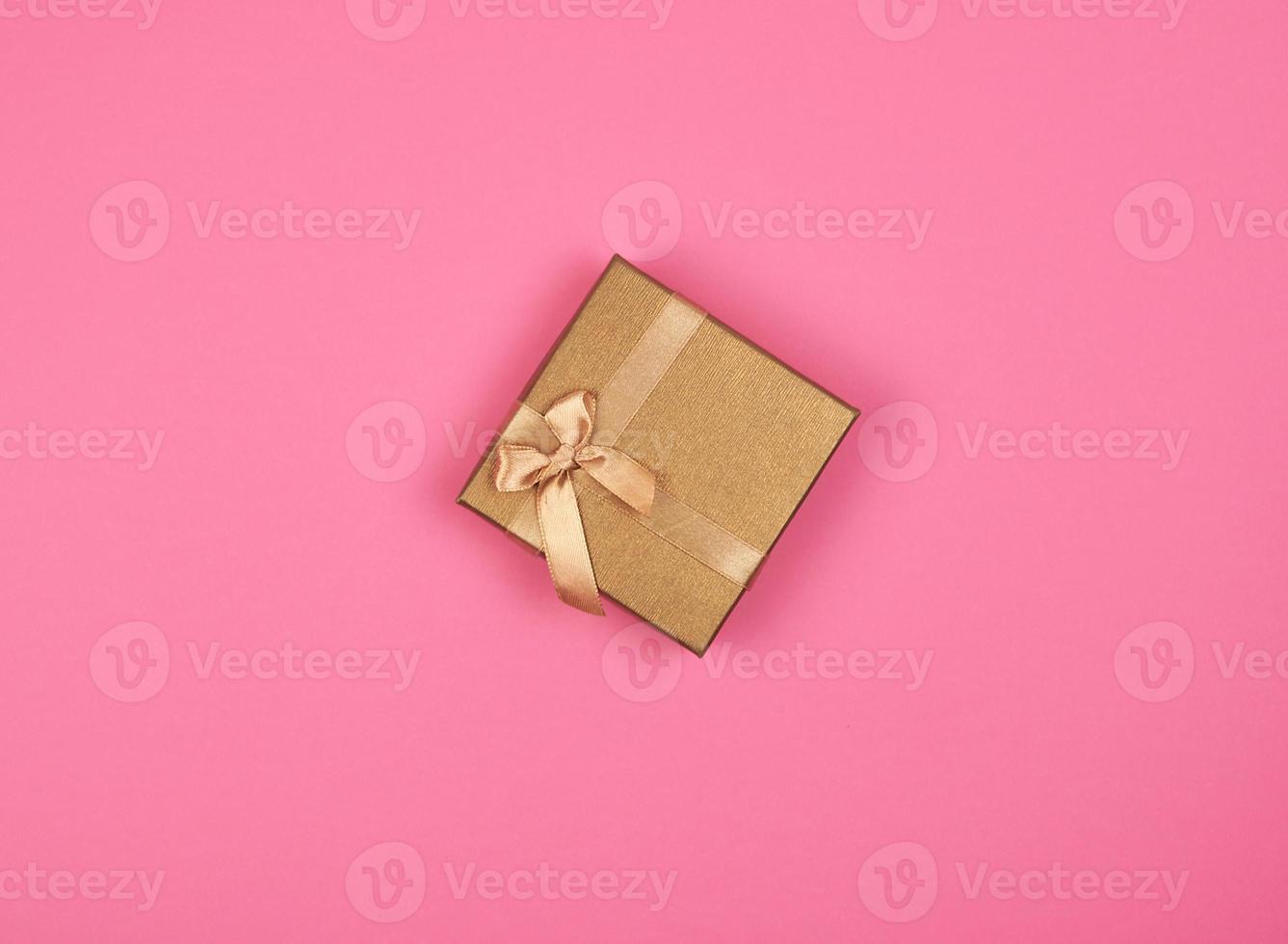 caja de regalo dorada cerrada con un lazo en un fondo rosa foto