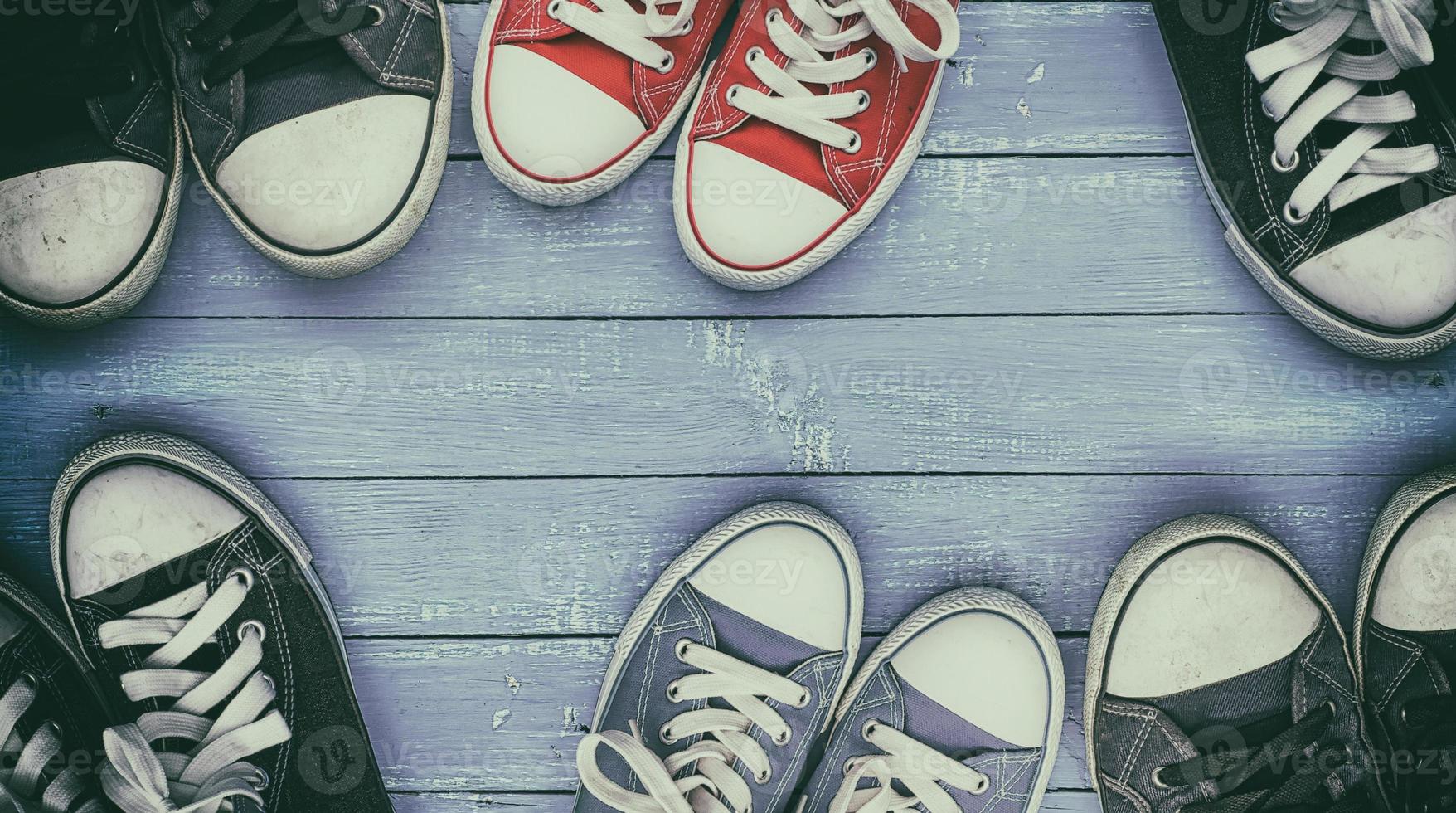 Six pairs of old, worn sneakers on a lilac wooden surface photo