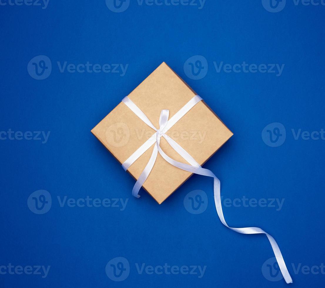 cardboard gift square box tied with a white thin ribbon on a dark blue background photo