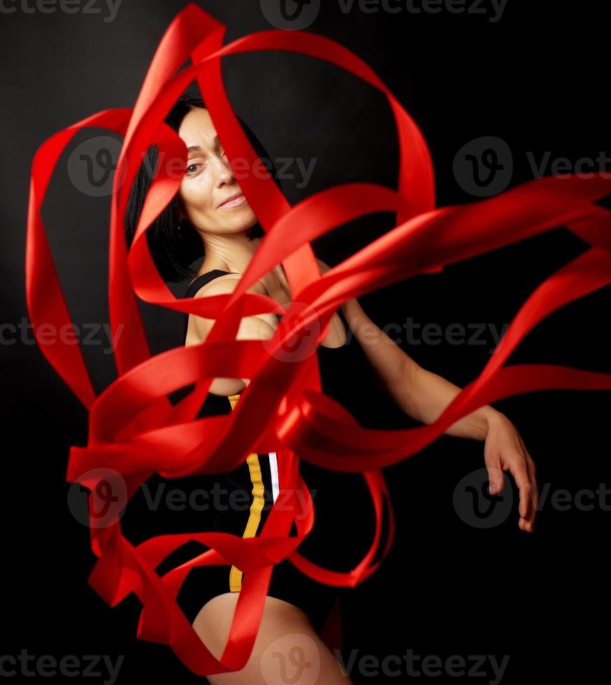 young woman gymnast of Caucasian appearance with black hair spins red satin ribbons photo