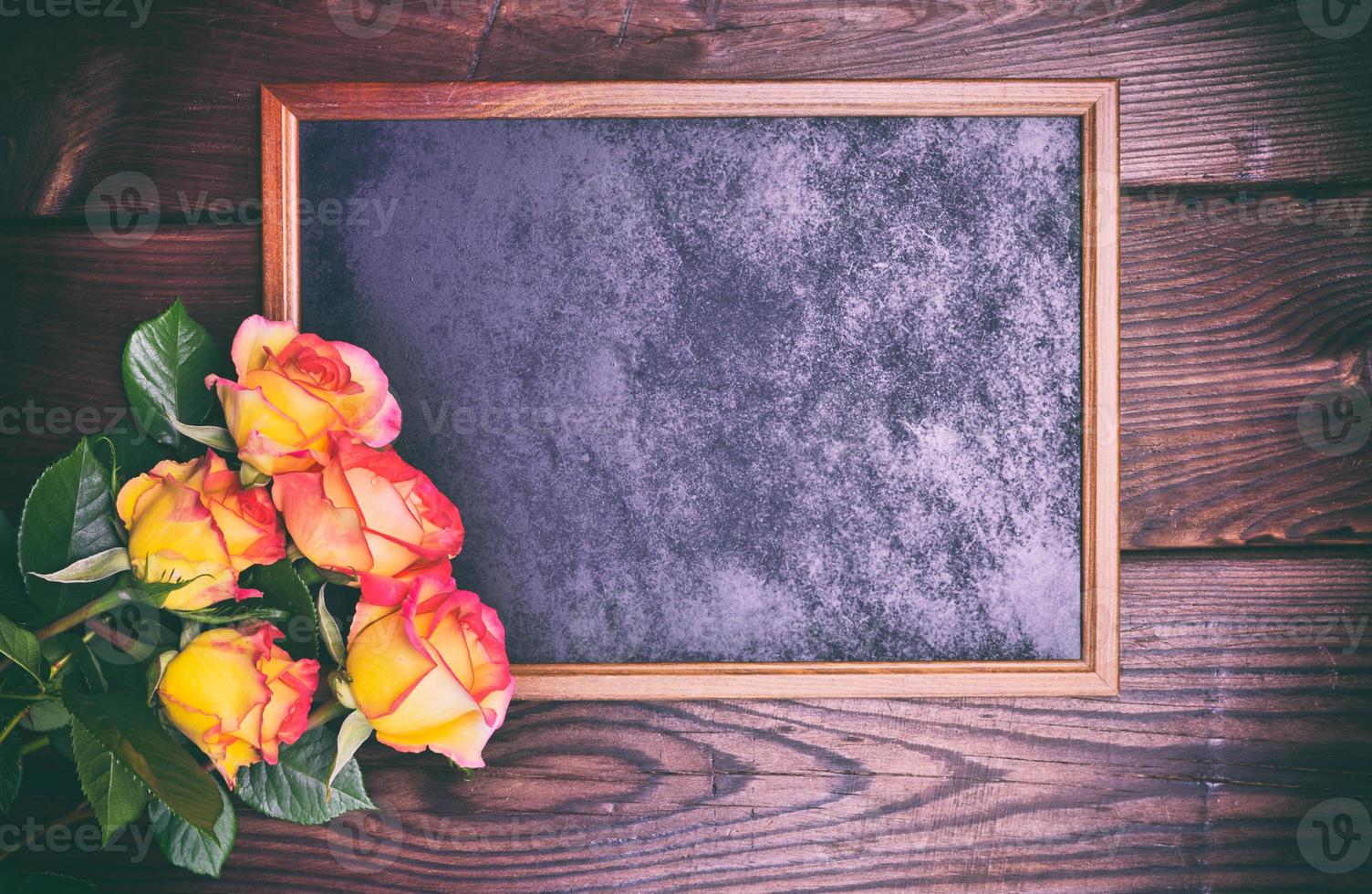 black wooden frame next to a bouquet of yellow roses photo