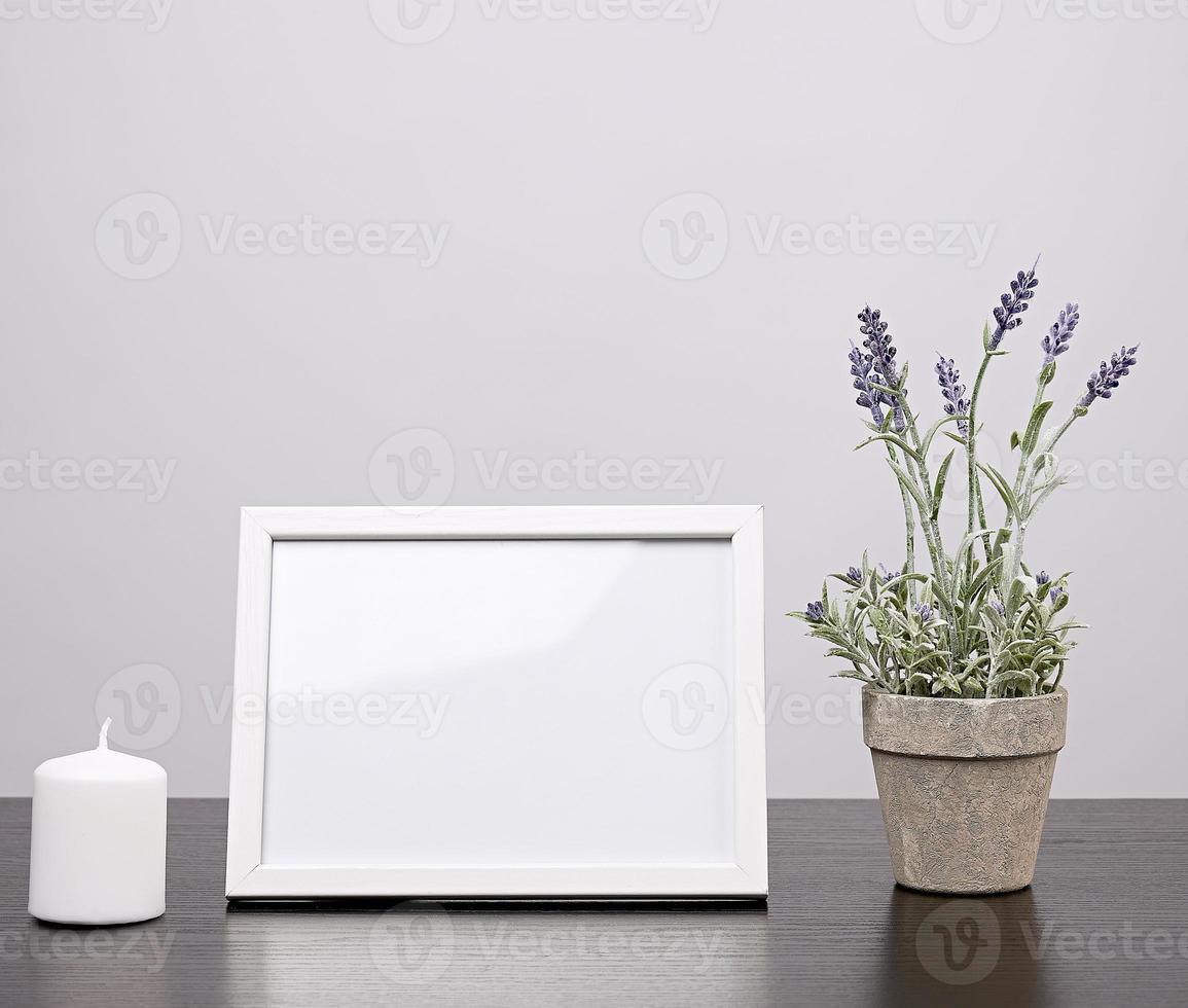 empty white frame, flowerpot with flower and candle on a black table photo