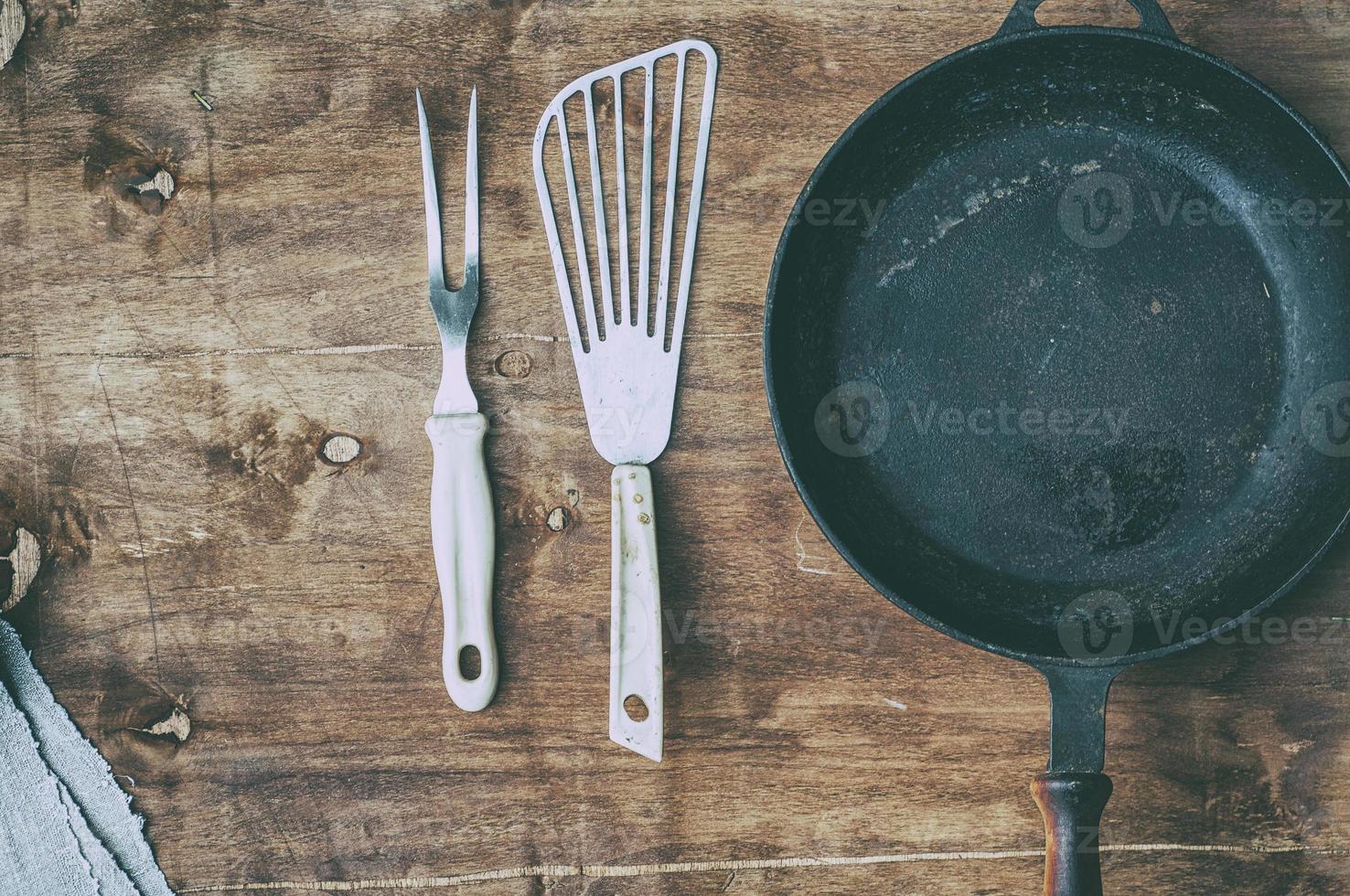 Empty black cast-iron frying pan with vintage kitchen items on a brown table photo