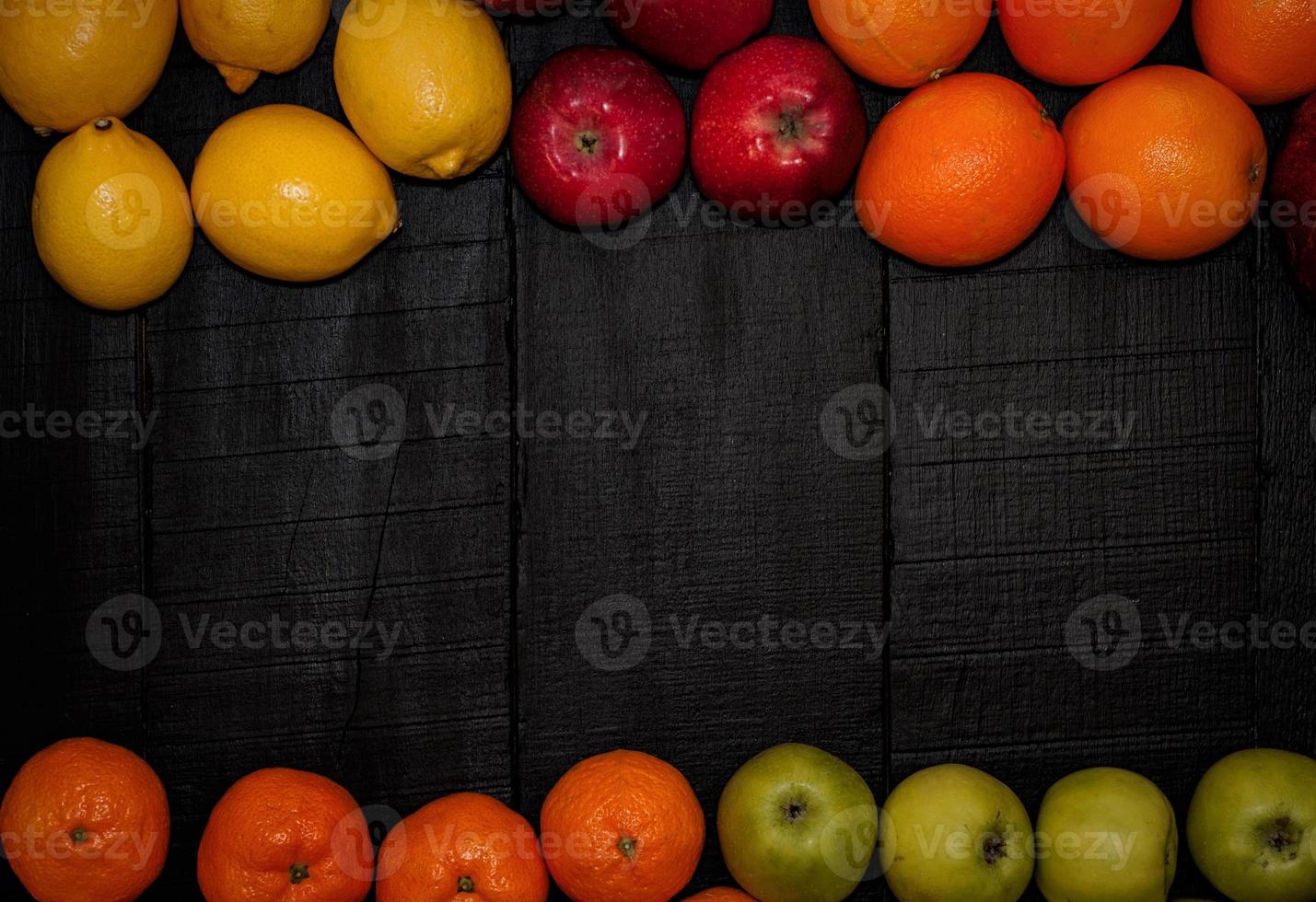 Ripe fruits are laid out on the perimeter on a black wooden background photo