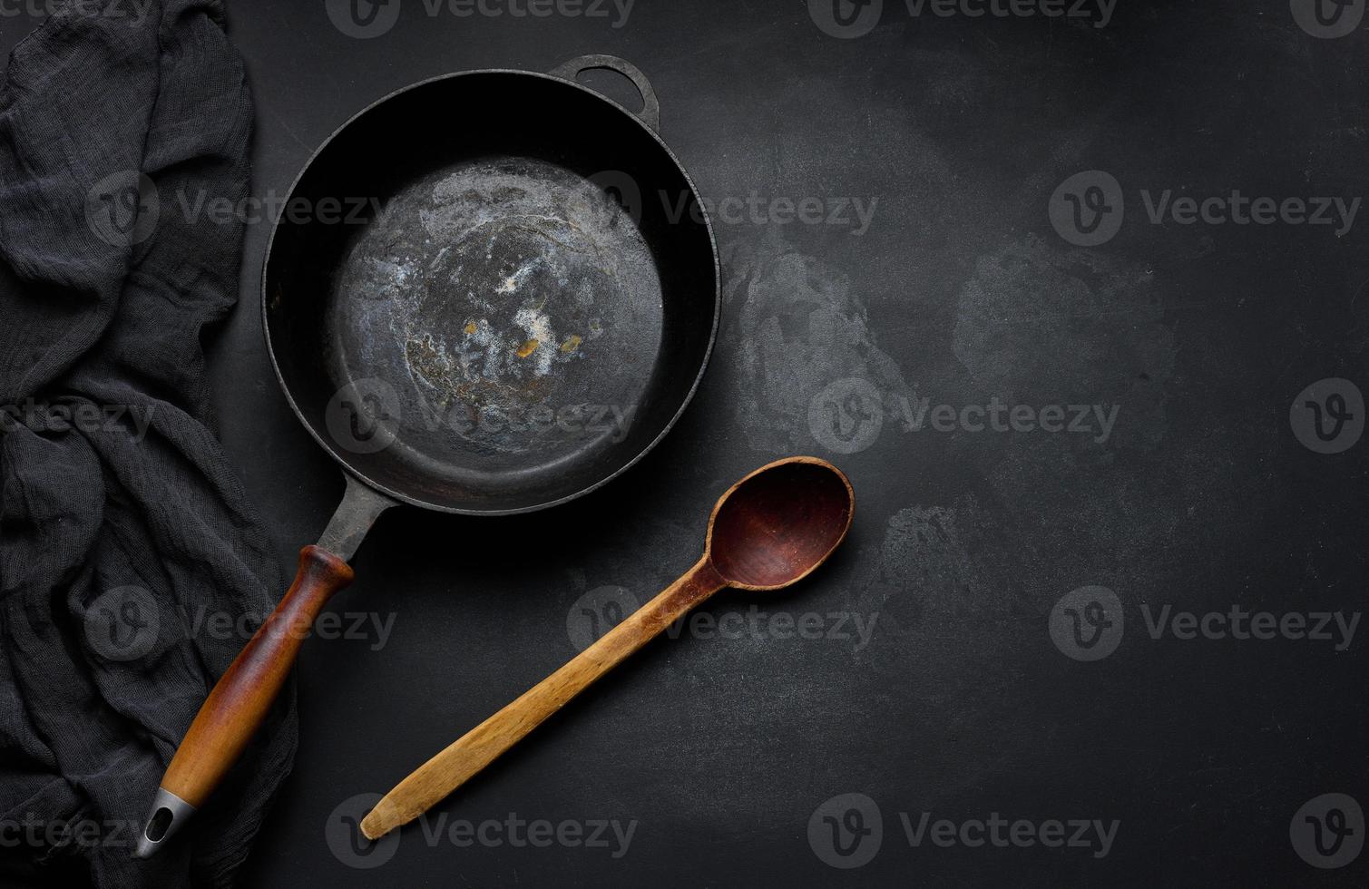 Empty round cast iron frying pan with wooden handle on black table, top view photo