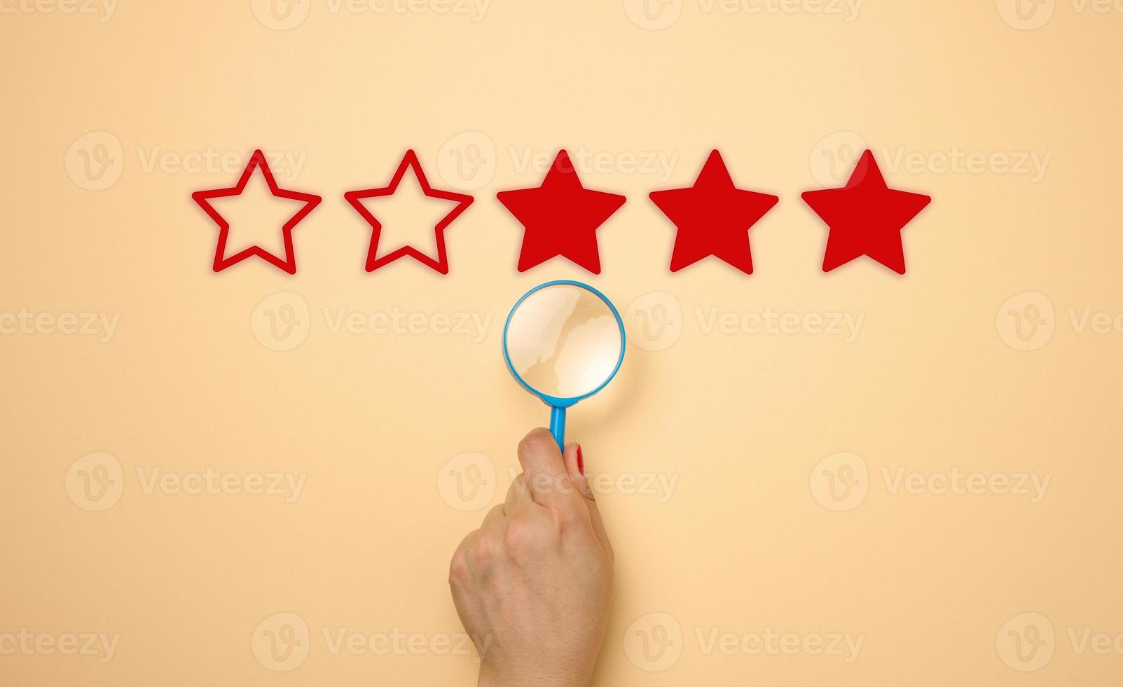 five stars and a hand with a blue plastic magnifier on a beige background. Evaluation of the quality of services and goods, high rating photo