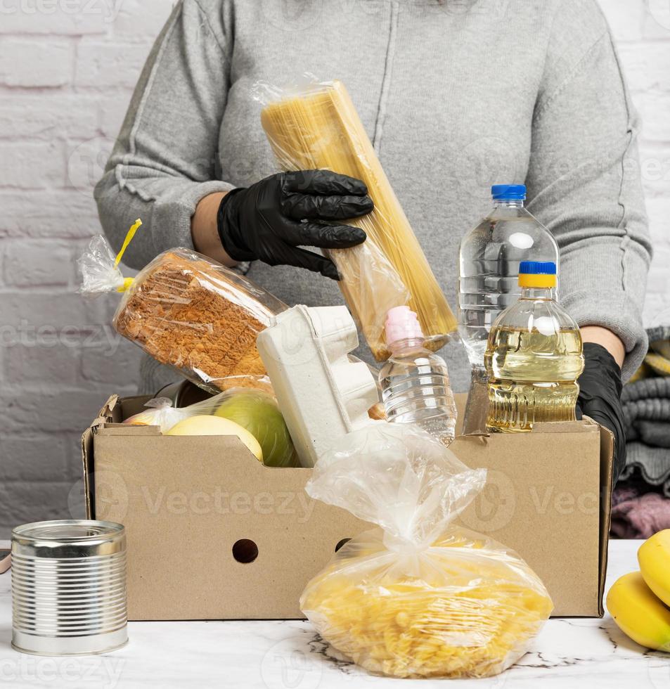 mujer en un suéter gris está empacando comida en una caja de cartón, el concepto de asistencia y voluntariado foto