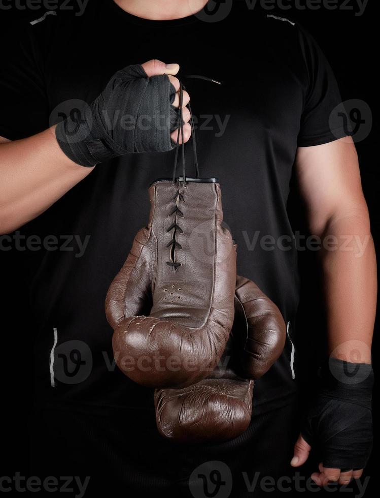 athlete in black clothes holds very old vintage leather brown boxing gloves photo