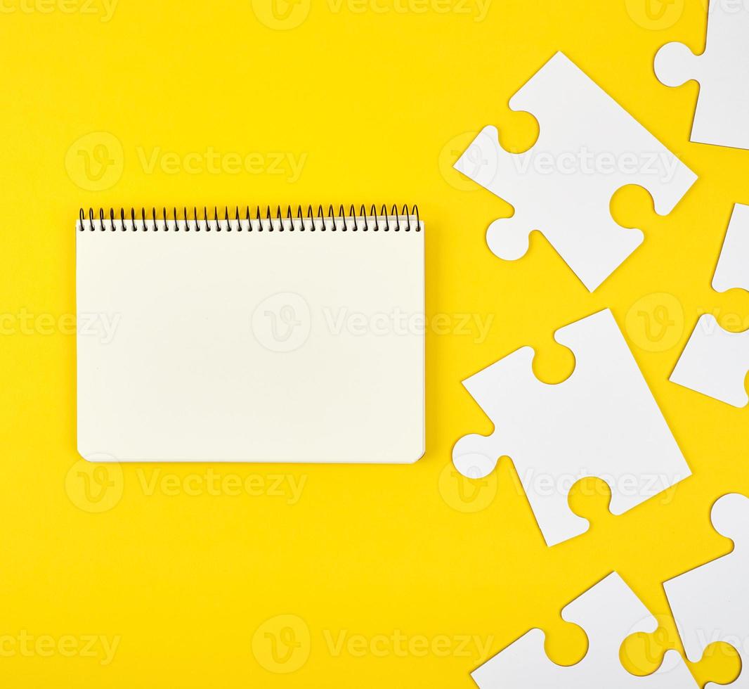 cuaderno abierto sobre un fondo amarillo, junto a grandes rompecabezas en blanco foto