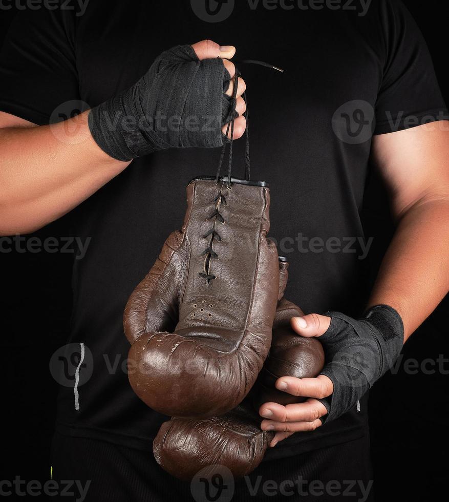 athlete in black clothes holds very old vintage leather brown boxing gloves photo