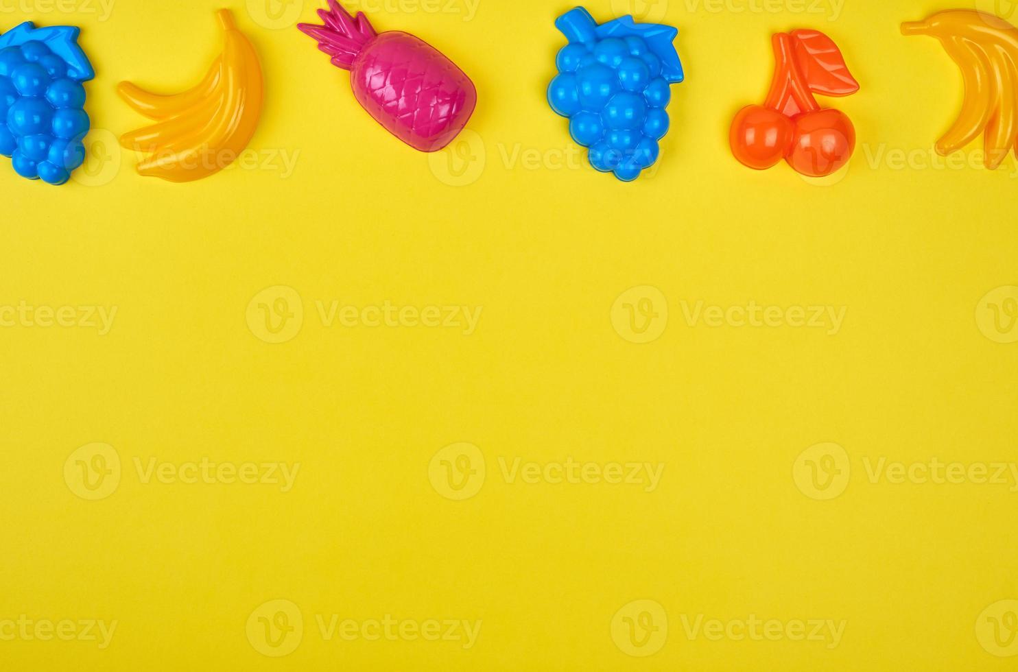 multicolored plastic toys fruits on a yellow  background photo