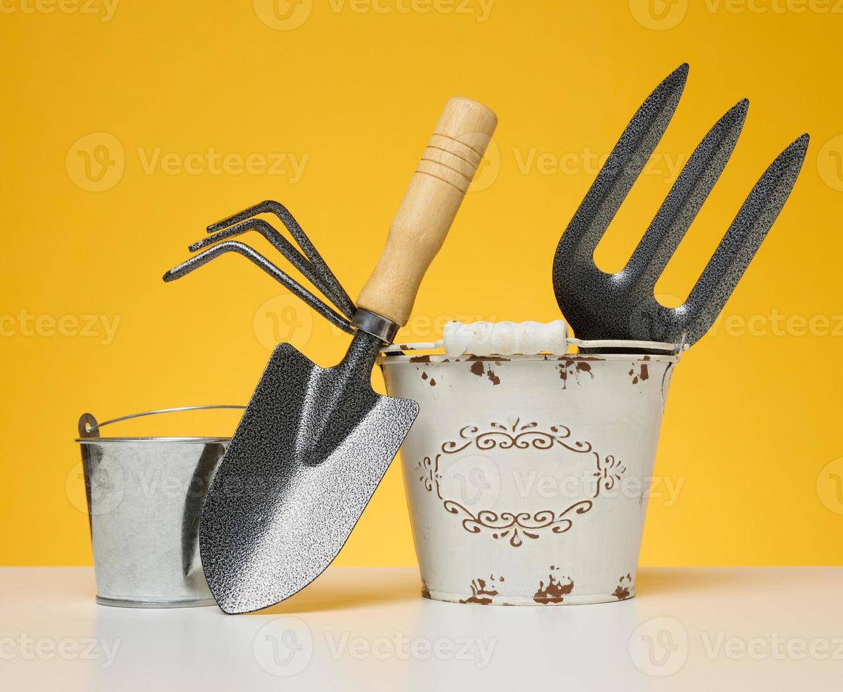 Miniature garden tools in a metal bucket on a yellow background photo