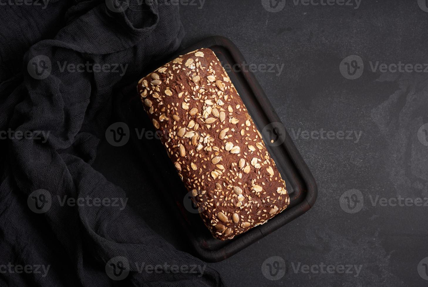 baked square rye flour bread with oatmeal on black background, top view photo